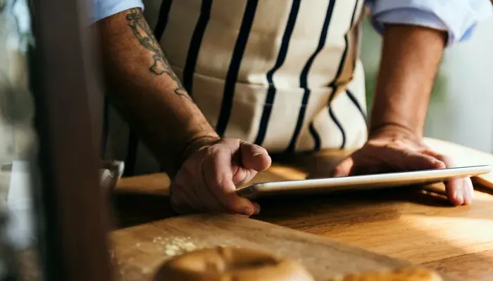 Owner in apron checks a tablet on a wooden counter with bagels, planning menus and orders for the local cafe